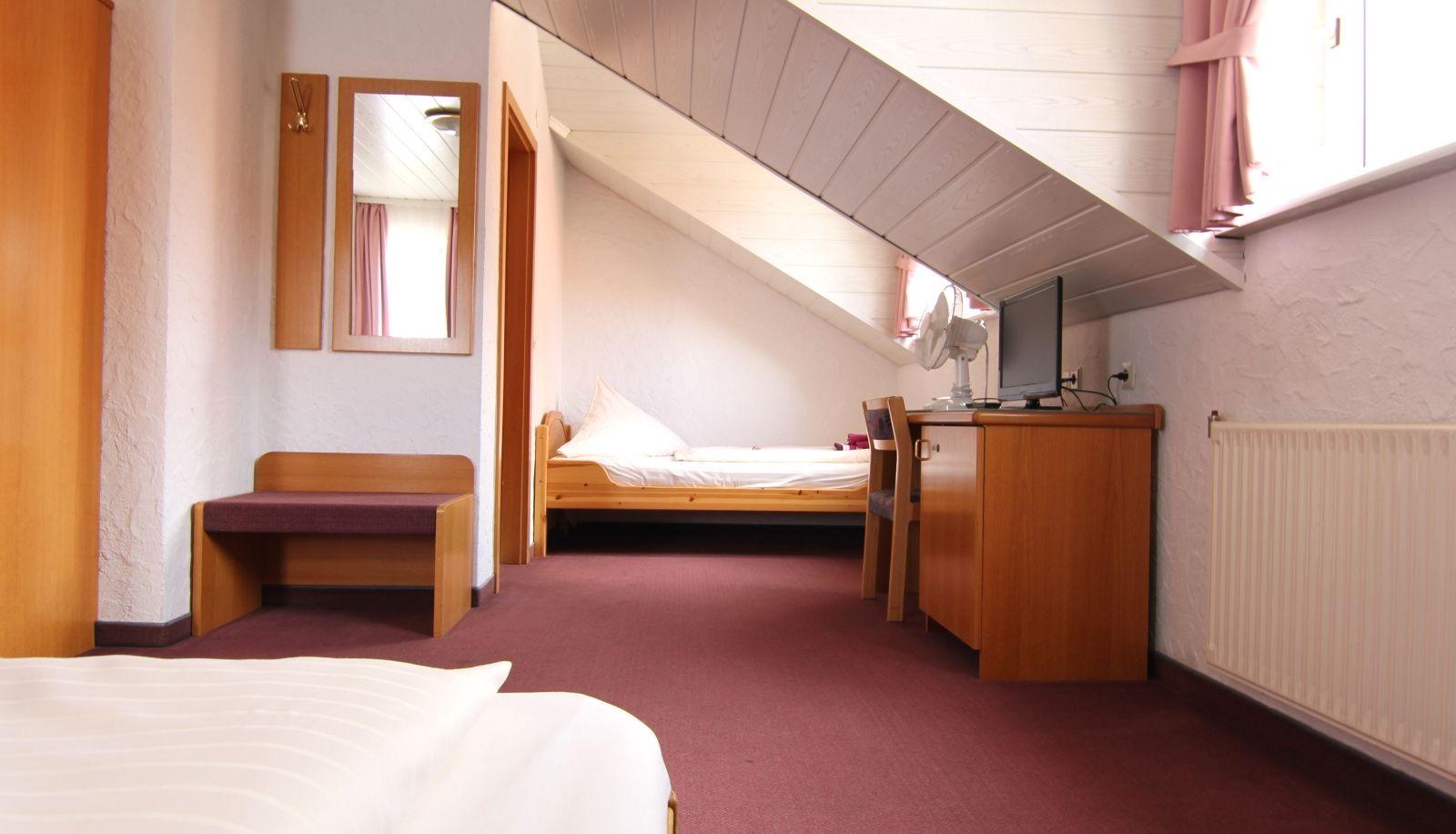 Zimmer unter dem Dach mit Einzelbett, Schreibtisch und Fernseher