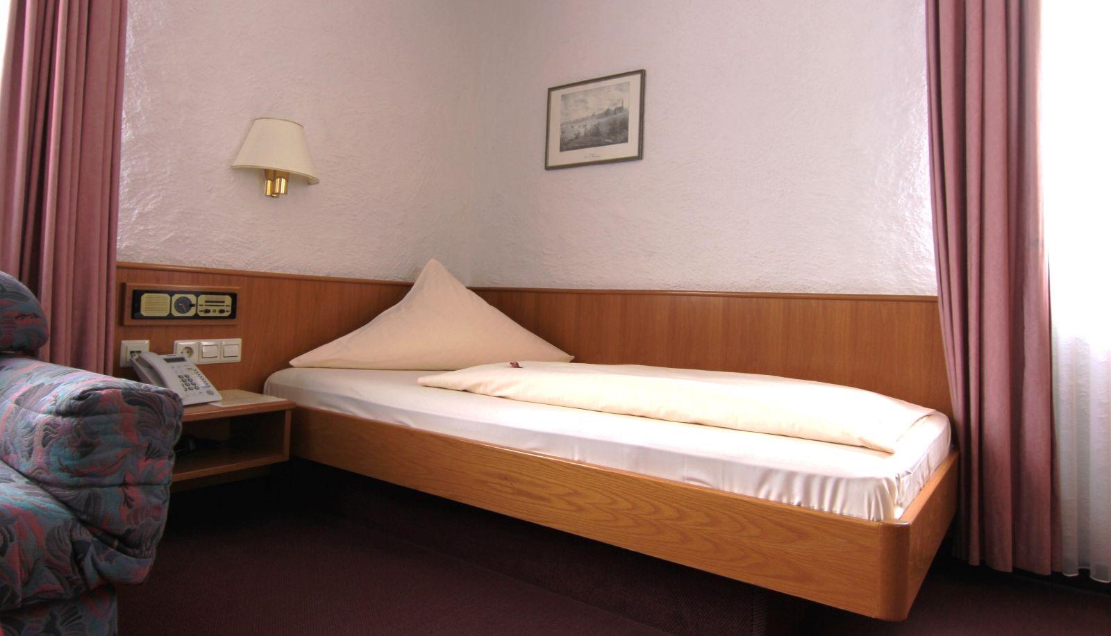Einzelzimmer mit Einzelbett, Nachttisch und Wandleuchte